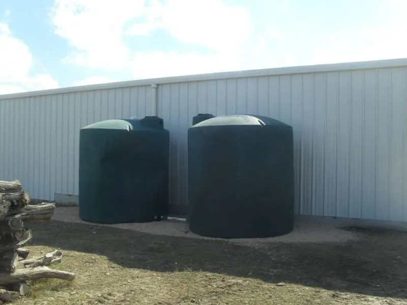 Twin rainwater storage tanks beside a white metal building.