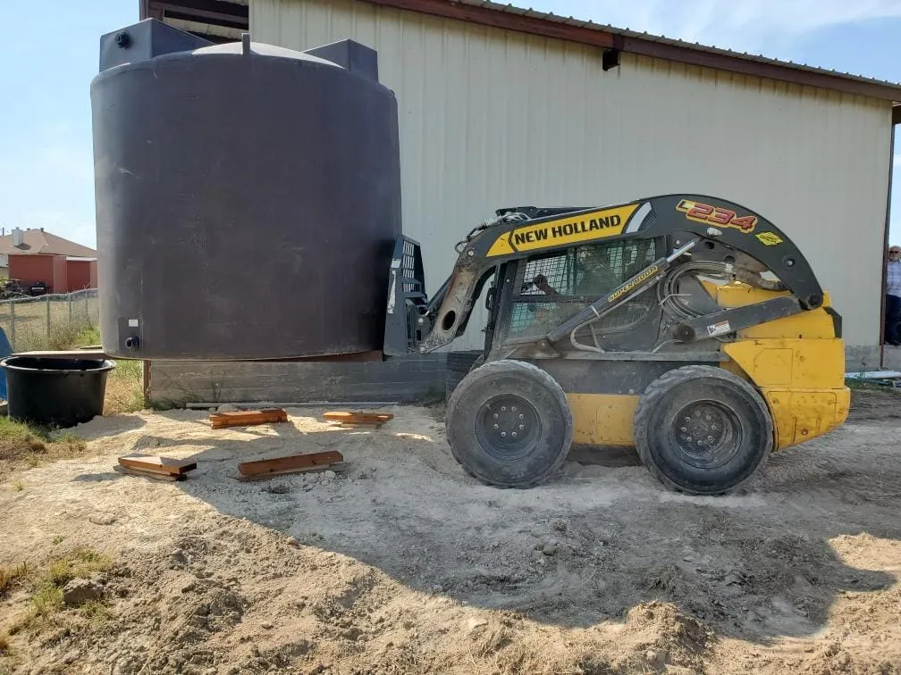 Skid steer setting a water storage tank during installation.