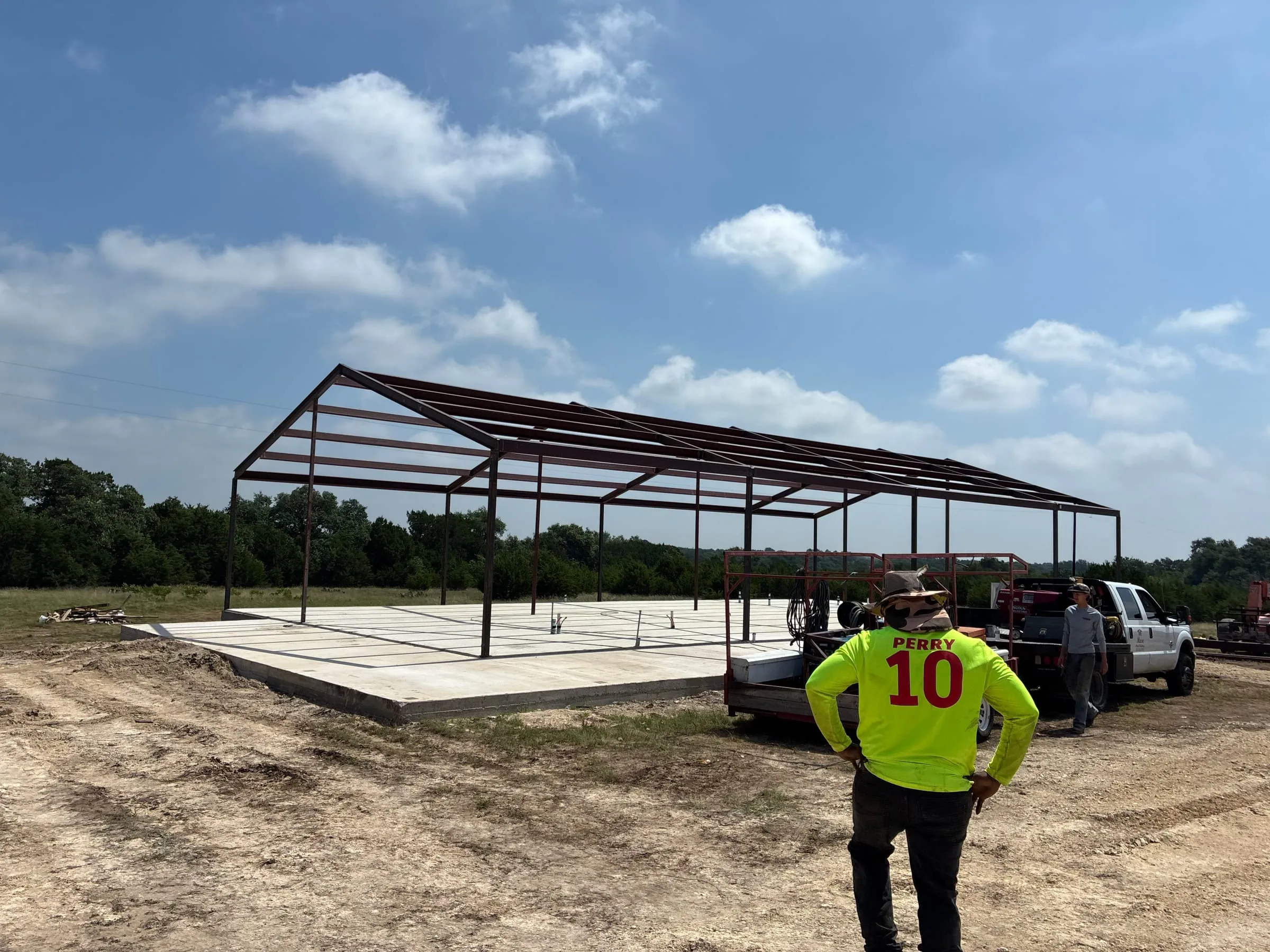 Steel home frame and crew positioned around the concrete slab.