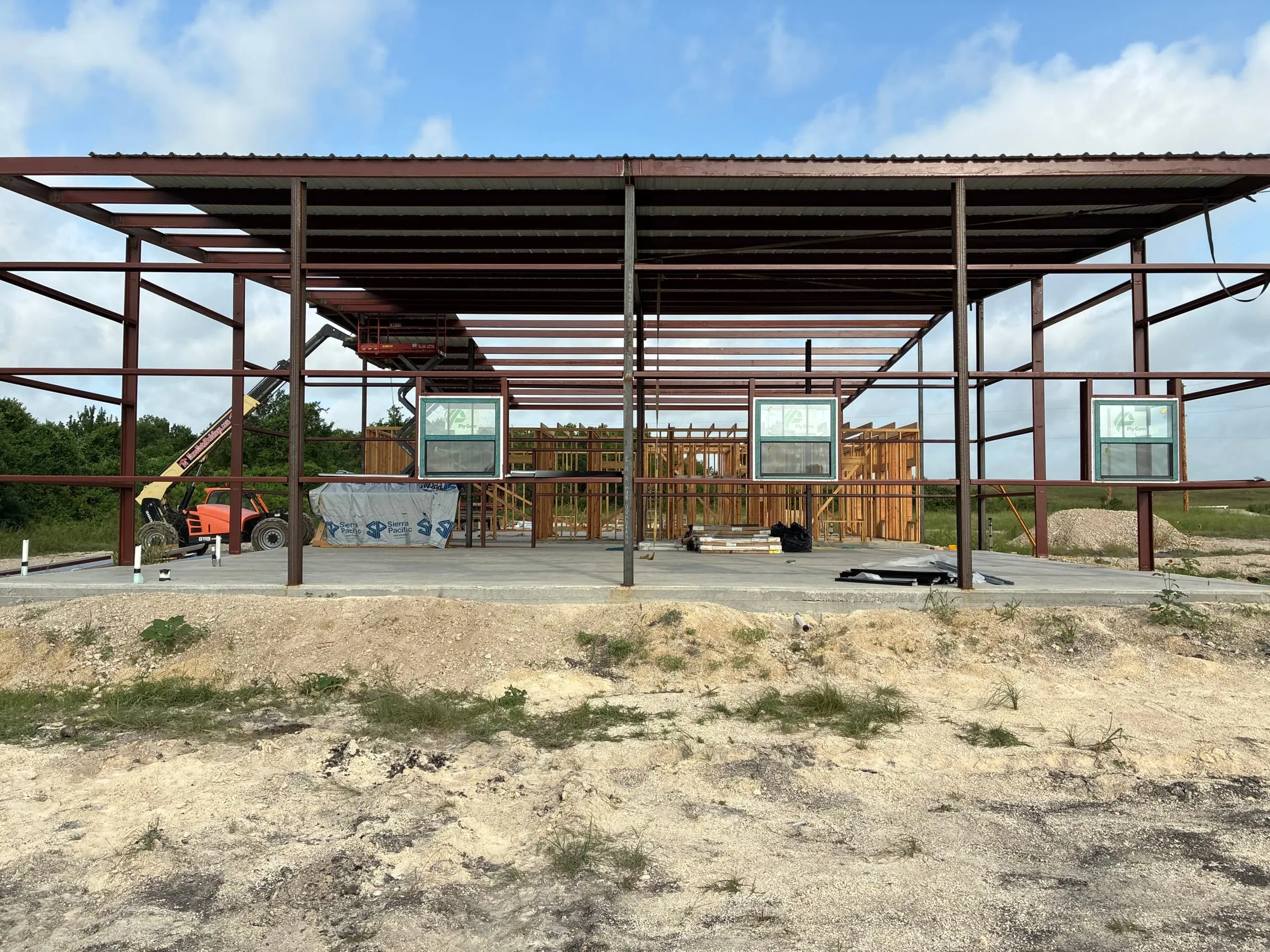 Roofed steel structure with wood wall framing taking shape below.