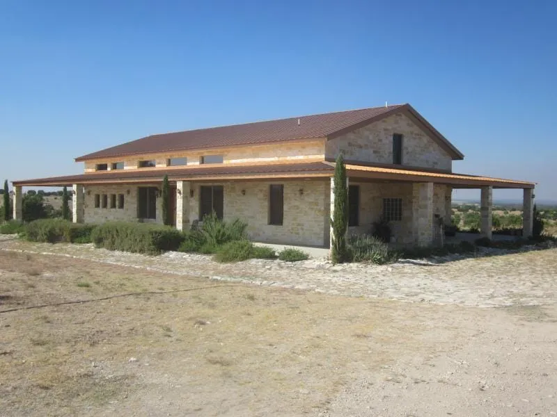 Stone ranch house with red metal roof and full-length covered porch.