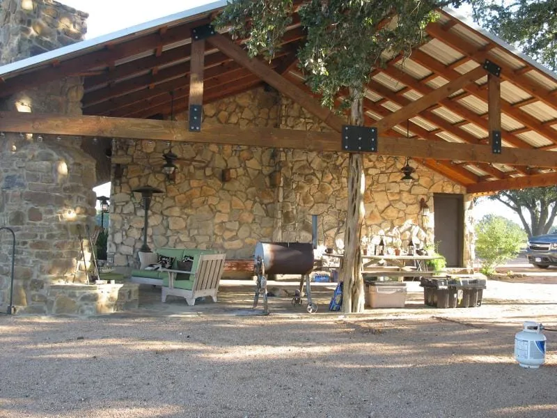 Stone outdoor kitchen pavilion with timber posts and metal roof.